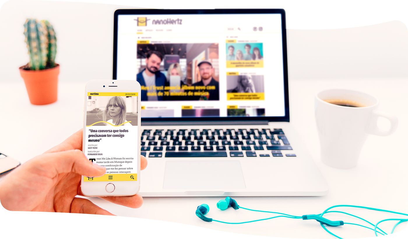 Person holding a phone with an article page shown on its page. The foreground has got a desktop with the home page opened.